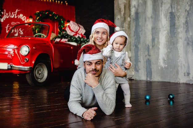 Fröhliche Eltern mit Tochter auf Weihnachtsmütze zu Hause mit Weihnachten