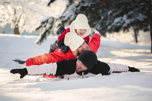 Fröhliche Eltern und Sohn liegen im Winter im Wald im Schnee.