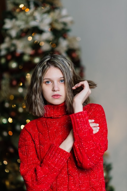 Fröhliche, emotional überraschte junge Frau am Weihnachtsbaum im gemütlichen Wohnzimmerkonzept des Glücks