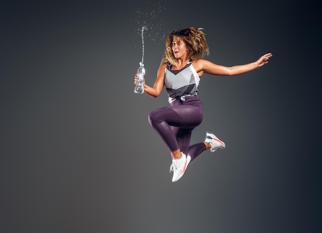 Fröhliche energetisierende Frau springt im Fotostudio mit Wasserballen, Spritzern.