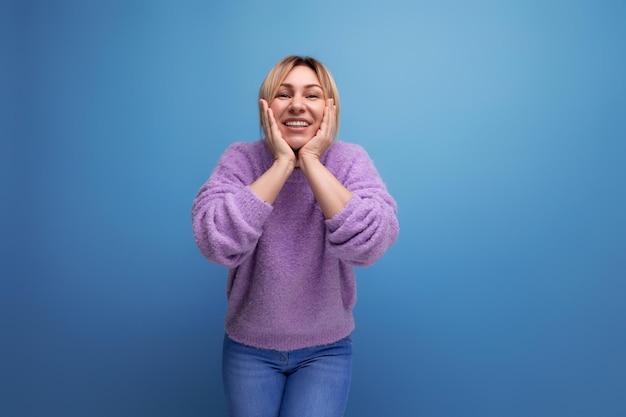 Fröhliche, energiegeladene blonde junge Beraterin in lila Pullover glücklich auf blauem Hintergrund mit Kopie