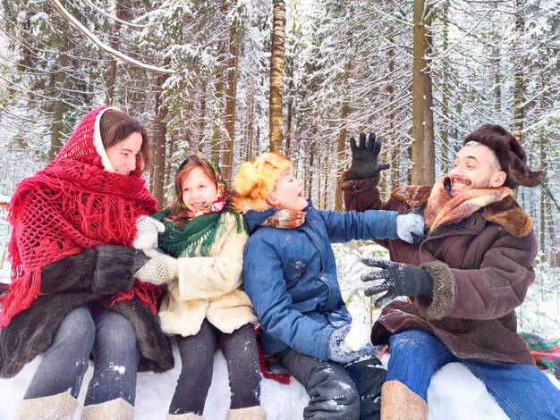 Fröhliche ethnische Familienkleidung mit Schalen und Ohrklappen in einem Winterwald im Karneval Maslenitsa in