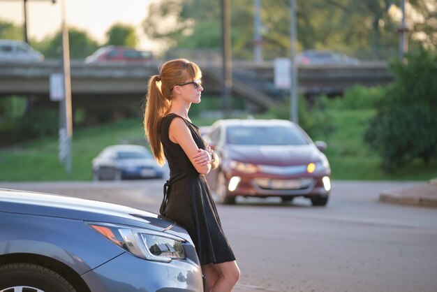 Fröhliche Fahrerin in lässigem Outfit, die einen warmen Tag in der Nähe ihres Autos auf einer Sommerstraße genießt Reise- und Transportkonzept