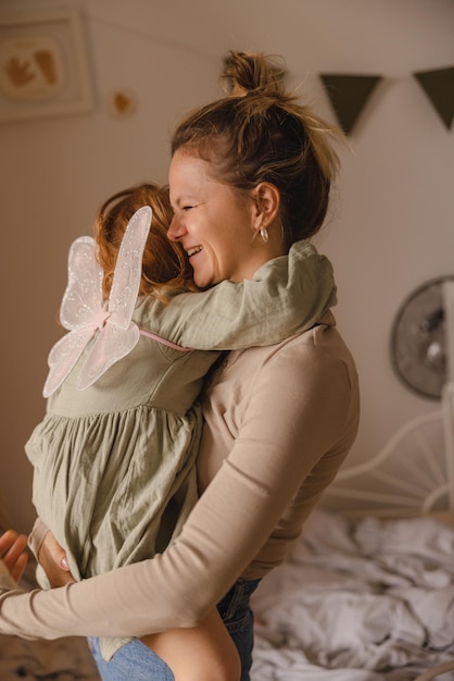 Fröhliche, fairhäutige junge Mutter, die das kleine Mädchen umarmt, das drinnen in den Armen hält Konzept der familiären Beziehungen