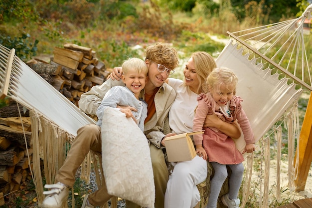 Fröhliche Familie, die Spaß auf der Hängematte hat, Sommercamping. Paare mit Kindern reisen im Campingwagen, in der Natur und im Wald im Hintergrund. Camping-Abenteuer, Reise-Lifestyle, Urlaub mit dem Wohnmobil