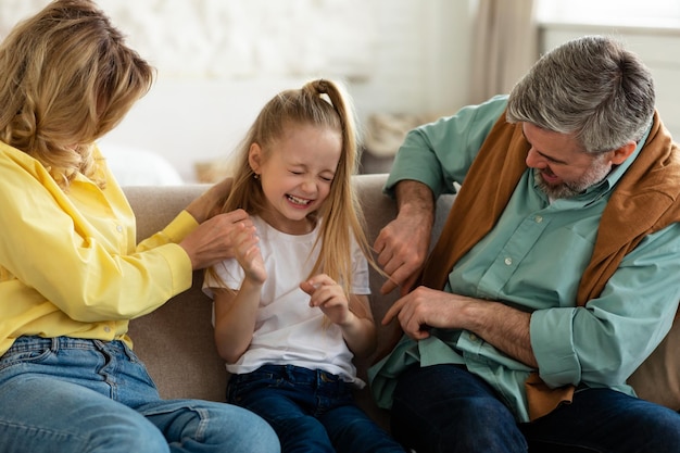 Fröhliche Familie, die Spaß hat, Eltern, die Tochter drinnen kitzeln