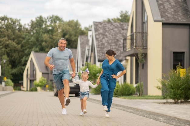 Fröhliche Familie. Fröhliche Eltern und Tochter beim Laufen, während sie abends Zeit draußen verbringen