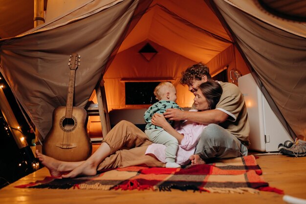 Fröhliche Familie mit schönem Baby beim Spielen und gemeinsame Zeit im Glamping am Sommerabend verbringen Luxus-Campingzelt für Erholung im Freien und Erholung Lifestyle-Konzept