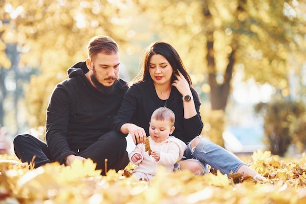 Fröhliche Familie sitzt auf dem Boden und hat Spaß zusammen mit ihrem Kind im schönen Herbstpark.