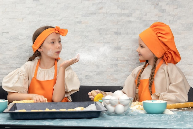 Fröhliche familienlustige mädchenkinder in orangefarbener kochuniform bereiten den teig backkekse im kit vor