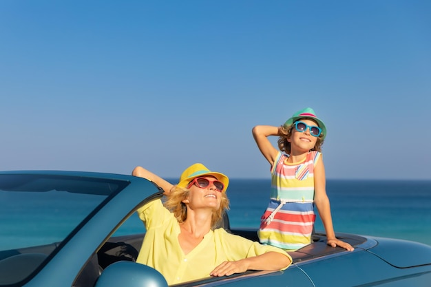 Fröhliche Familienreise mit dem Auto am Meer Mutter und Kind amüsieren sich im blauen Cabriolet Sommerurlaubskonzept