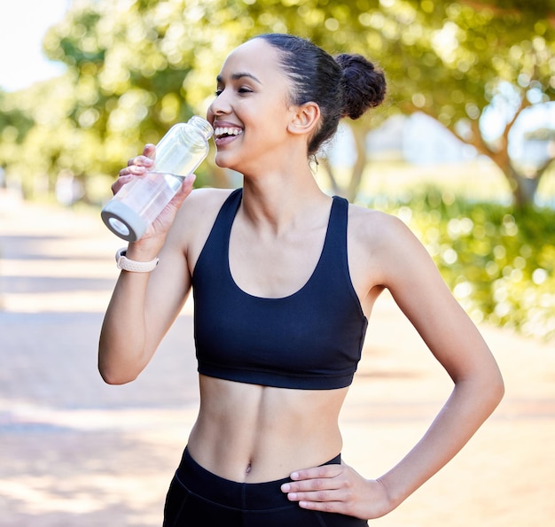 Fröhliche Fitness-Frau und Lachen mit einer Wasserflasche in der Ruhepause vom lustigen Lauftraining oder Cardio-Training im Park. Fitte aktive oder durstige Sportlerin oder Läuferin mit einem Lächeln für Nachhaltigkeit