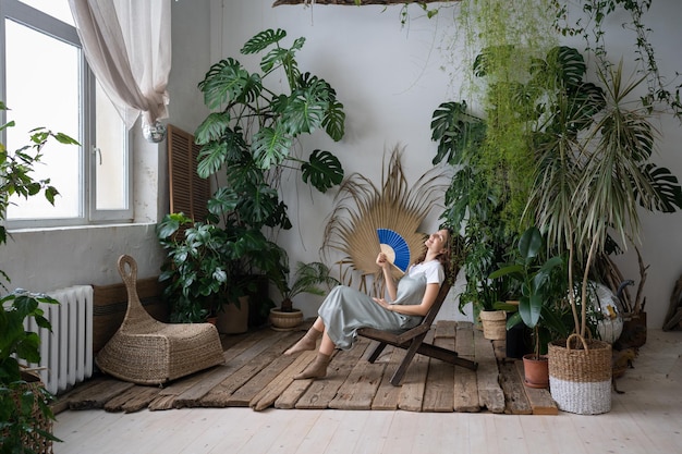 Foto fröhliche floristin, die sich im hausgarten erfrischt und frische luft atmet, halten papierfächer in der hand an heißen tagen