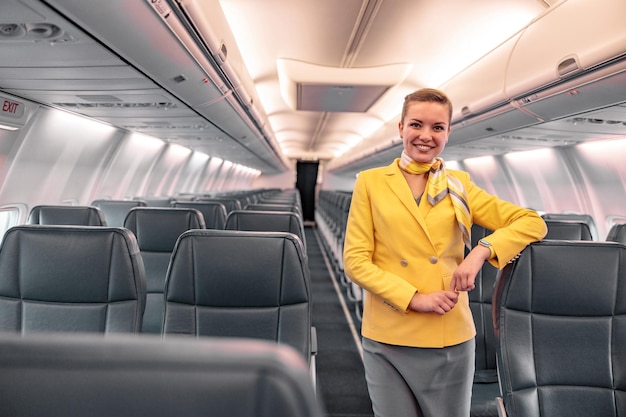 Fröhliche Flugbegleiterin, die in die Kamera schaut und lächelt, während sie ihre Hand auf den Beifahrersitz legt