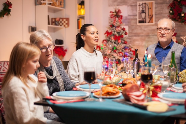 Fröhliche Frau am Tisch mit ihrer Familie beim Weihnachtsessen.