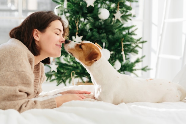 Fröhliche Frau bekommt Kuss vom Lieblingshund, hält die Augen vor Vergnügen geschlossen