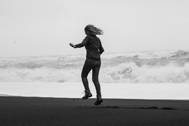 Fröhliche Frau, die am Strand von Reynisfjara springt, monochrome Landschaftsfotografie