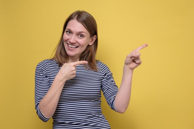 Fröhliche Frau, die auf Copyspace an der gelben Wand beiseite zeigt
