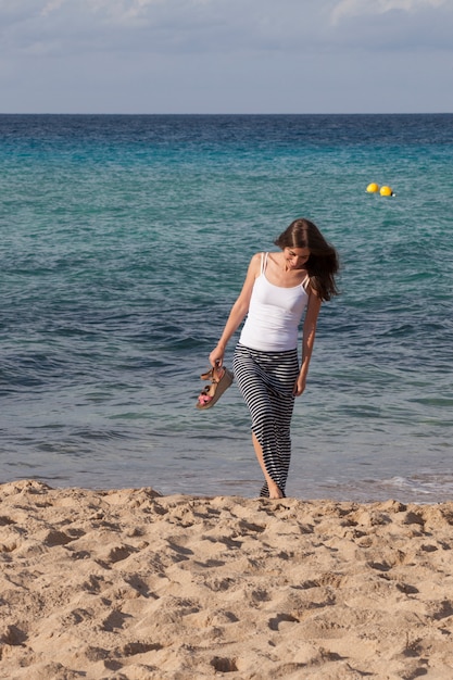 Foto fröhliche frau, die auf dem strand geht, der ihre sandalen hält