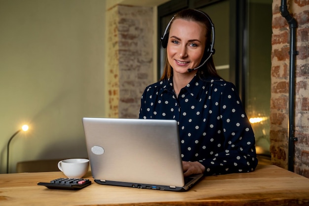 Fröhliche Frau, die ein Headset trägt und mit einem Laptop lacht, der Online-Bildungs- und Unterhaltungskonzept für glückliche ethnische Mädchen unterrichtet