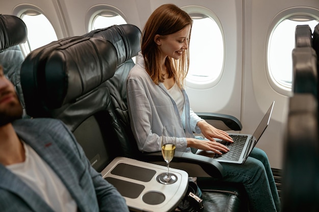 Fröhliche Frau, die im Flugzeug an einem Notebook arbeitet