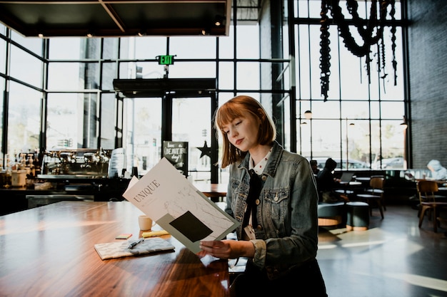 Fröhliche Frau, die in einem Café eine Zeitschrift liest