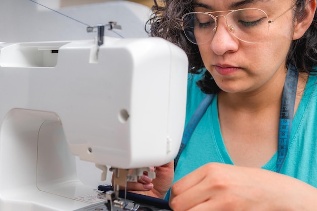 Fröhliche Frau, die näht, während sie an ihrem Arbeitsplatz in der Modewerkstatt sitzt