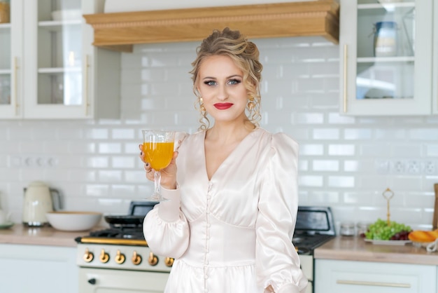 Fröhliche Frau, die Orangensaft trinkt und in der Nähe des Küchentisches steht