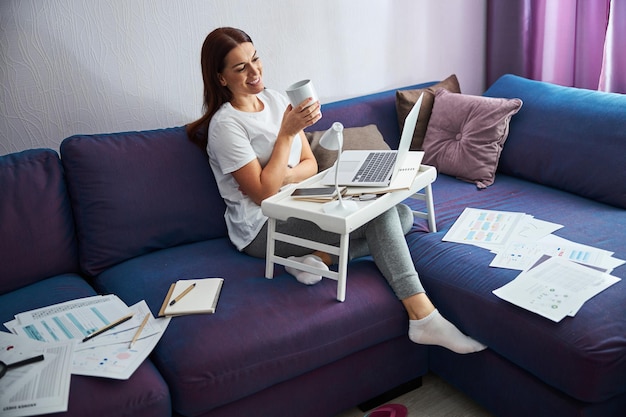 Fröhliche Frau, die während des Arbeitstages zu Hause Tee trinkt