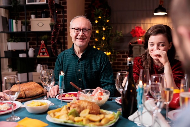 Fröhliche Frau, die Weihnachten mit der Familie feiert und am festlichen Esstisch mit Papa zu Hause lacht. Vater und Tochter essen gemeinsam Weihnachtsgerichte, lächeln, haben Spaß, schauen in die Kamera