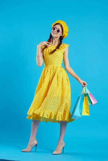 Fröhliche Frau gelbes Kleid Einkaufsspaß blauer Hintergrund