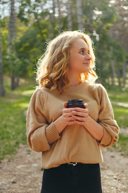 Fröhliche Frau hält eine Tasse Kaffee fest, während sie in einem Park steht