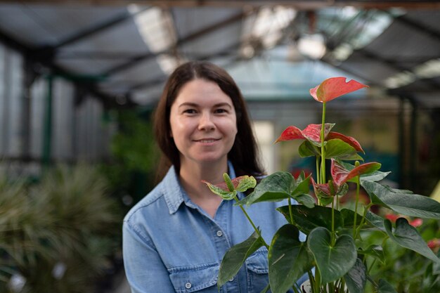 Fröhliche Frau im Gewächshaus mit rotem Anthurium im Topf