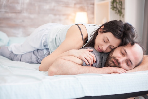 Fröhliche Frau im Schlafanzug, die mit ihrem Freund auf einem bequemen Bett schläft.