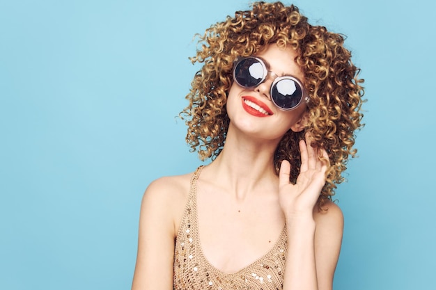 Fröhliche Frau lächelt, rote Lippen, lockiges Haar, blauer Hintergrund, Sonnenbrille, beschnittene Ansicht