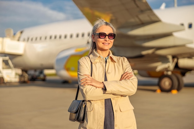 Fröhliche Frau mit Sonnenbrille, die draußen am Flughafen steht