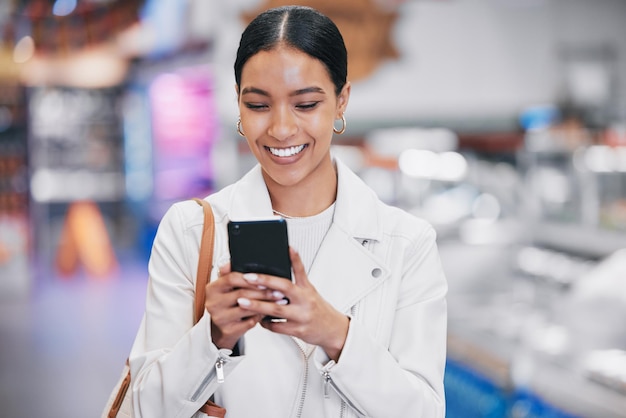 Fröhliche Frau mit Telefon, die lustige Social-Media-Meme im Internet liest, während sie in einem Einkaufszentrum ist. Frau mit einem Lächeln, während sie nach dem Einzelhandelseinkauf einen Rabattcoupon oder eine SMS an einen Kontakt auf einem mobilen Smartphone sendet