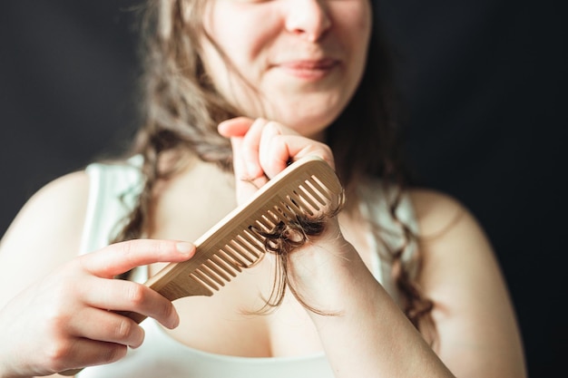 Fröhliche Frau pflegt ihr Haar mit einem Holzkamm. Haarspliss-Behandlung, tägliche Routine und Rituale für perfektes und strahlendes langes Haar