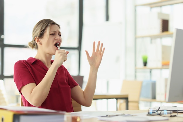 Fröhliche Frau singt am Arbeitsplatz mit Stift als Mikrofon