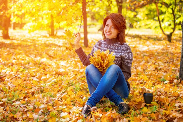 Fröhliche Frau sitzt auf gelben Blättern