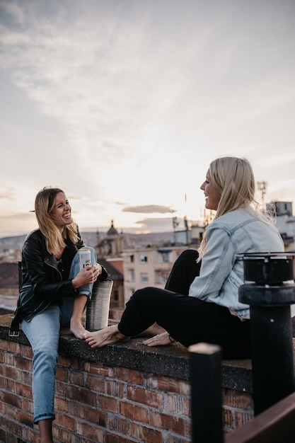 Fröhliche Frauen sprechen, während sie auf der Terrasse gegen den Himmel sitzen