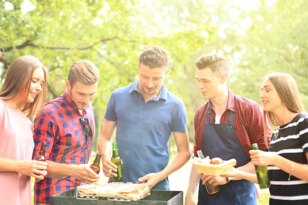 Fröhliche Freunde, die Fleisch grillen und eine Grillparty im Freien genießen.