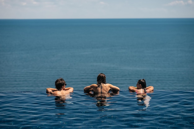 Fröhliche Freunde, die im Infinity-Pool gegen die Küste schwimmen