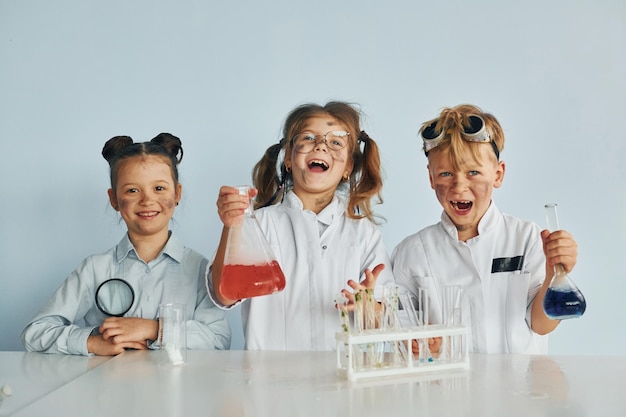 Fröhliche Freunde lächeln Kinder in weißen Kitteln spielen Wissenschaftler im Labor, indem sie Geräte verwenden