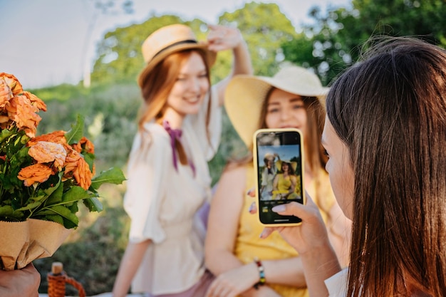 Fröhliche Freundinnen, die ein Selfie auf dem Smartphone machen und beim Picknick in der Sommerparkgruppe gen genießen