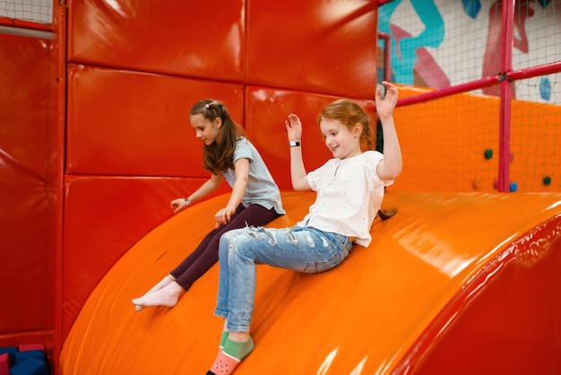 Fröhliche Freundinnen spielen im Unterhaltungszentrum zwischen weichen Würfeln. Mädchenfreizeit im Urlaub, Kinderglück, glückliche Kinder auf dem Spielplatz