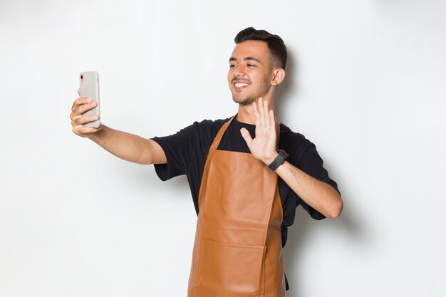 Fröhliche, fröhliche Barista-Kellnerin des jungen Mannes mit mobilem Smartphone isoliert auf weißem Hintergrund