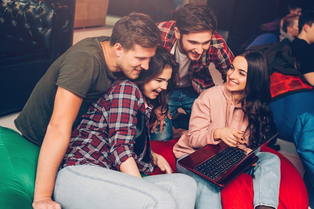 Fröhliche fröhliche Menschen sitzen zusammen im Spielzimmer. Sie schauen zusammen auf den Laptop. Die Leute lächeln.