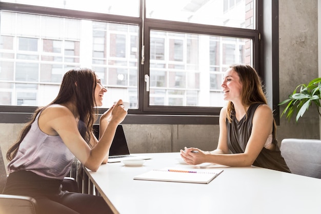 Fröhliche Geschäftsfrauen diskutieren am Schreibtisch im Büro