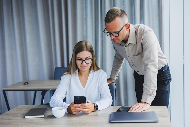 Fröhliche Geschäftsleute, die einen Laptop in einem Büro verwenden Glücklich lächelnde junge Unternehmer bei der Zusammenarbeit in einem modernen Arbeitsbereich Zwei junge Geschäftsleute, die zusammen an einem Tisch sitzen